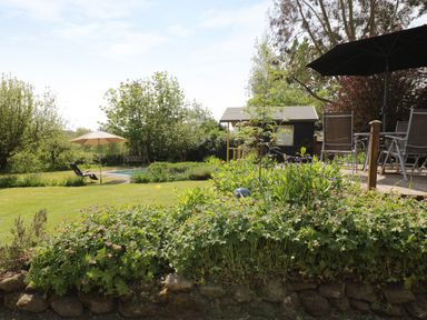 A garden with a lawn chairs umbrellas a wooden shed and flowering plants at Rhydygaled in Llanrhaeadr-Ym-Mochnant