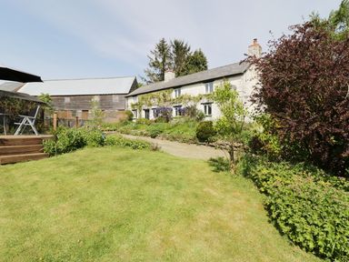 A garden with green lawn trees and flower beds next to a white house and a wooden shed at Rhydygaled in Llanrhaeadr-Ym-Mochnant