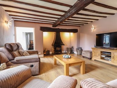 A living room with wooden beams on the ceiling a wood burning stove sofas a wooden coffee table and a television on a wooden stand at Rhydygaled in Llanrhaeadr-Ym-Mochnant