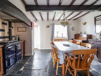 A dining room with a table and wooden chairs next to a piano and a stove at Rhydygaled in Llanrhaeadr-Ym-Mochnant