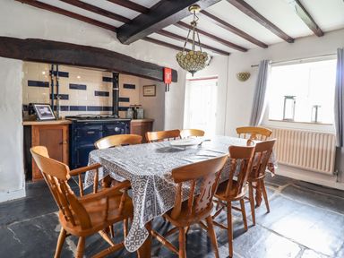 A dining room with wooden chairs around a table covered with a patterned tablecloth and a stove in the background at Rhydygaled in Llanrhaeadr-Ym-Mochnant