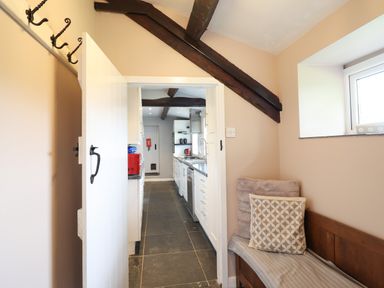 A hallway with wooden bench and cushions leading to a kitchen with white cabinets and exposed wooden beams at Rhydygaled in Llanrhaeadr-Ym-Mochnant