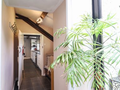 A narrow hallway with a hanging light and open door leading to a kitchen with white cabinets and black floor tiles at Rhydygaled in Llanrhaeadr-Ym-Mochnant