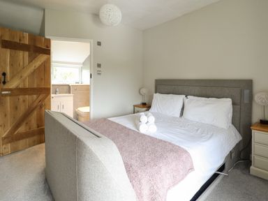 A bedroom with a gray upholstered bed white bedding a mauve blanket rolled white towels bedside tables with lamps and an open wooden door leading to a bathroom at Rhydygaled in Llanrhaeadr-Ym-Mochnant