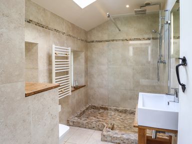 A bathroom with a walk-in shower with glass screen a white sink on a wooden stand and a white towel radiator at Rhydygaled in Llanrhaeadr-Ym-Mochnant