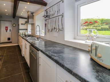 A kitchen with dark countertops white cabinets hanging utensils a sink and window with a glass vase and toaster at Rhydygaled in Llanrhaeadr-Ym-Mochnant