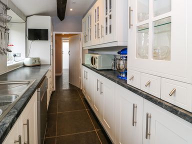 A galley kitchen with white cabinets black countertops appliances and a sink at Rhydygaled in Llanrhaeadr-Ym-Mochnant