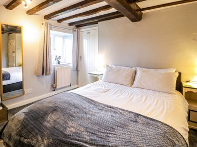A bedroom with a bed with white pillows and a gray blanket exposed wooden beams a mirror and a window at Rhydygaled in Llanrhaeadr-Ym-Mochnant
