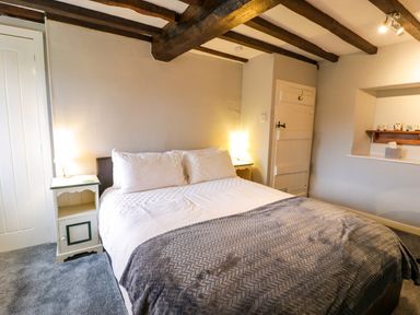 A bedroom with a bed bedside tables lamps exposed wooden ceiling beams and a small shelf with items at Rhydygaled in Llanrhaeadr-Ym-Mochnant
