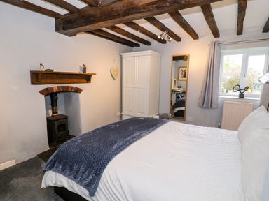 A bedroom with exposed wooden beams a bed with white bedding and a blue throw a white wardrobe a full length mirror and a window at Rhydygaled in Llanrhaeadr-Ym-Mochnant