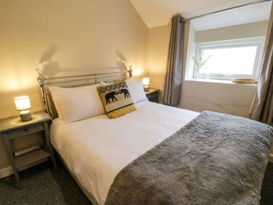 A bedroom with a bed white sheets a gray blanket bedside tables lamps a window with curtains and decorative pillows at Rhydygaled Llanrhaeadr-Ym-Mochnant