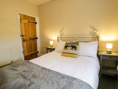 A bedroom with a bed with white bedding and an elephant pillow two bedside tables with lamps and a wooden door at Rhydygaled in Llanrhaeadr-Ym-Mochnant