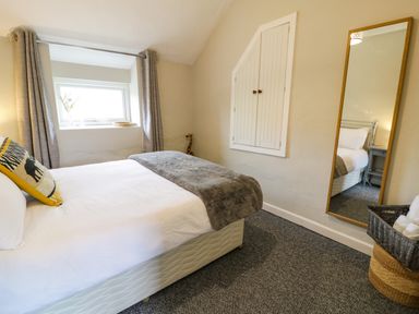 A bedroom with a white bed a mirror on the wall and a window with curtains at Rhydygaled in Llanrhaeadr-Ym-Mochnant