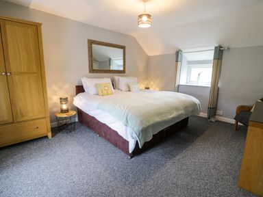 A bedroom with a double bed two bedside tables a wooden wardrobe and a window with curtains at Rhydygaled in Llanrhaeadr-Ym-Mochnant