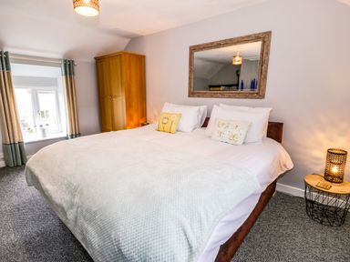 A bedroom with a large bed two pillows a wooden wardrobe a window with curtains and a side table with a lamp at Rhydygaled in Llanrhaeadr-Ym-Mochnant