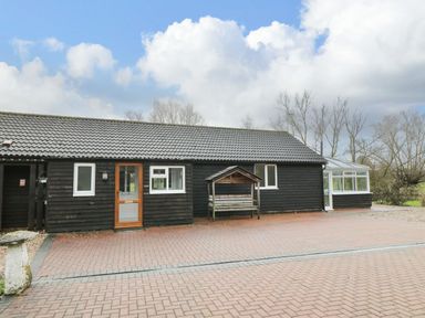 A black wooden building with a tiled roof and a paved area in front at The Annex in Royal Wootton Bassett