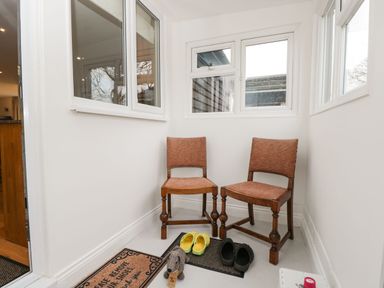 A small entryway with two wooden chairs brown mats and pairs of shoes at The Annex in Royal Wootton Bassett