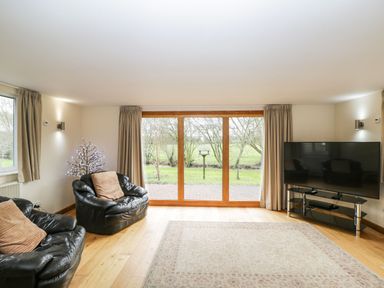 A living room with leather armchairs a television on a stand and sliding glass doors opening to a garden at The Annex in Royal Wootton Bassett