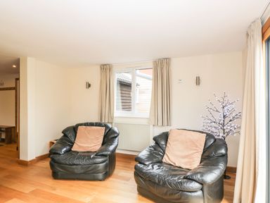 A room with two black leather armchairs each with a brown cushion and a window with beige curtains at The Annex in Royal Wootton Bassett