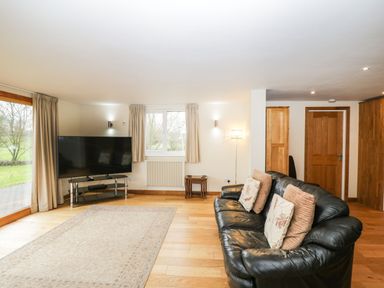 A living room with a black leather sofa and a large flat screen tv on a stand at The Annex in Royal Wootton Bassett