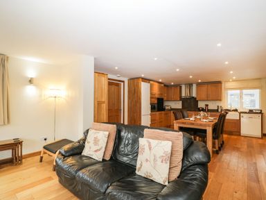 An open living room and kitchen with wooden cabinets a black leather sofa and a dining table at The Annex in Royal Wootton Bassett