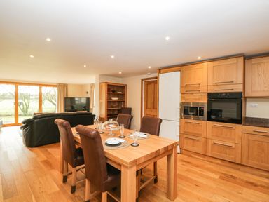 An open plan kitchen and dining area with wooden furniture brown chairs and a black sofa near a large window at The Annex in Royal Wootton Bassett