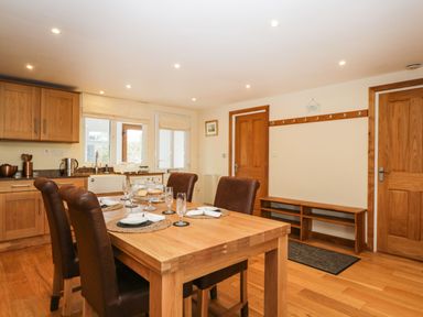 A dining area with a wooden table set with glasses and plates next to a kitchen with wooden cabinets at The Annex in Royal Wootton Bassett