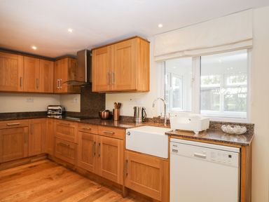 A kitchen with wooden cabinets a white sink a dishwasher a toaster and a window at The Annex in Royal Wootton Bassett