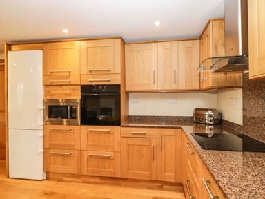 A kitchen with wooden cabinets a white refrigerator a built in microwave a built in oven a toaster and an electric cooktop at The Annex in Royal Wootton Bassett