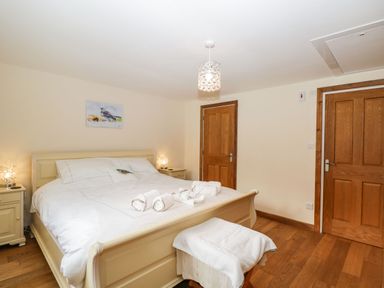 A bedroom with a bed white linens bedside tables lamps two wooden doors and wooden floor at The Annex in Royal Wootton Bassett