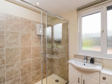 A bathroom with a glass shower enclosure tiled walls and a sink under a frosted window at The Annex in Royal Wootton Bassett