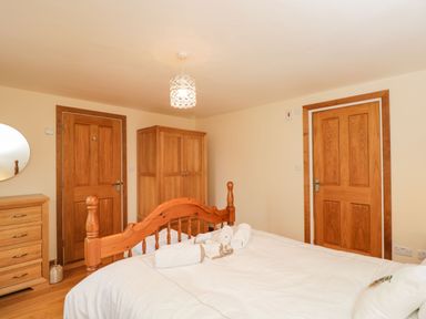 A bedroom with a wooden bed a chest of drawers wardrobe and two wooden doors at The Annex in Royal Wootton Bassett