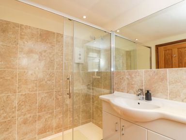 A bathroom with a glass enclosed shower and a white sink with cabinets at The Annex in Royal Wootton Bassett