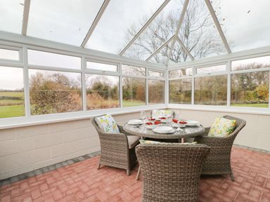 A conservatory with a round glass table and four wicker chairs with cushions at The Annex in Royal Wootton Bassett