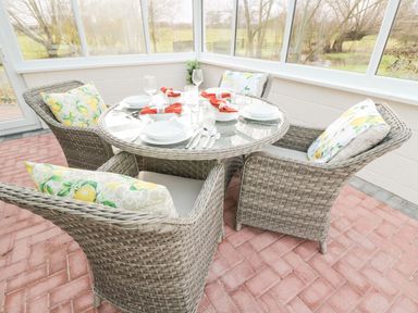 A dining area with a round glass table set with plates and glasses and wicker chairs with cushions at The Annex in Royal Wootton Bassett