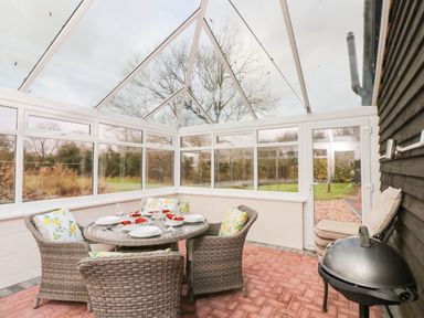 A dining area with a round table and four chairs inside a glass conservatory at The Annex in Royal Wootton Bassett
