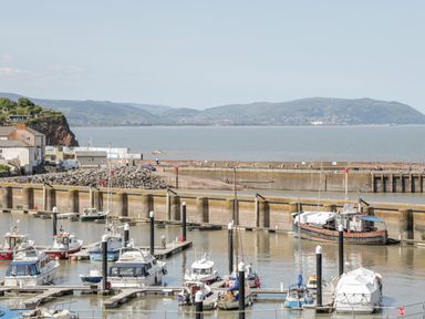 A marina with boats docked and a breakwater with hills in the background at The Old Byres in Washford near Watchet