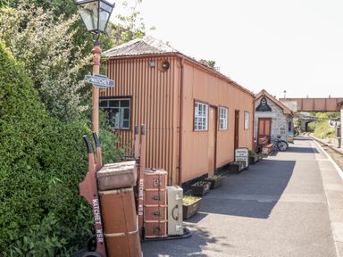 A railway platform with luggage trolleys and a brown building with windows and signs at The Old Byres in Washford near Watchet
