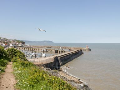 A coastal town with a harbor promenade boats and a lighthouse near the sea at The Old Byres in Washford near Watchet
