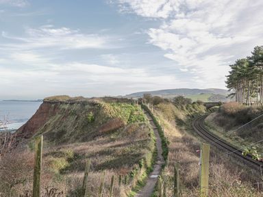 A coastal path beside a railway track with trees and hills in the background at The Old Byres in Washford near Watchet