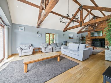 A living room with exposed wooden beams a fireplace and multiple sofas at The Old Byres in Washford near Watchet