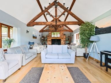 A living room with sofas a fireplace wooden beams and a piano at The Old Byres in Washford near Watchet