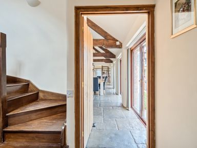 A hallway with stone flooring wooden beams and doors leading to a dining area at The Old Byres in Washford near Watchet