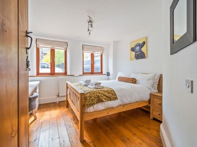 A bedroom with a wooden bed and bedside table two windows and a painting of a cow at The Old Byres in Washford near Watchet