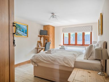 A bedroom with a double bed two folded towels on the bed a bedside table with a lamp a desk with a chair a wall-mounted TV and a window at The Old Byres in Washford near Watchet