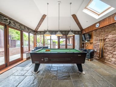 A games room with a pool table and chairs near large windows and a stone floor at The Old Byres in Washford near Watchet