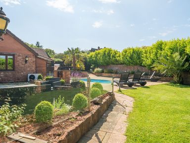 A backyard with a swimming pool lounge chairs and green plants at The Old Byres in Washford near Watchet