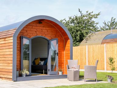 A wooden pod with open glass doors showing a sofa inside and two patio chairs with a table outside at Withy Willows Diddlebury near Ludlow