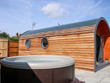 A hot tub outside a wooden pod with circular windows at Withy Willows in Diddlebury near Ludlow