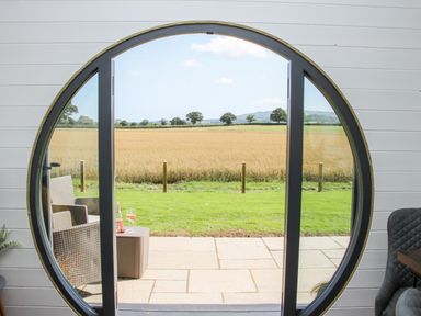 A circular window opening to a patio with chairs and drinks overlooking a field at Withy Willows in Diddlebury near Ludlow